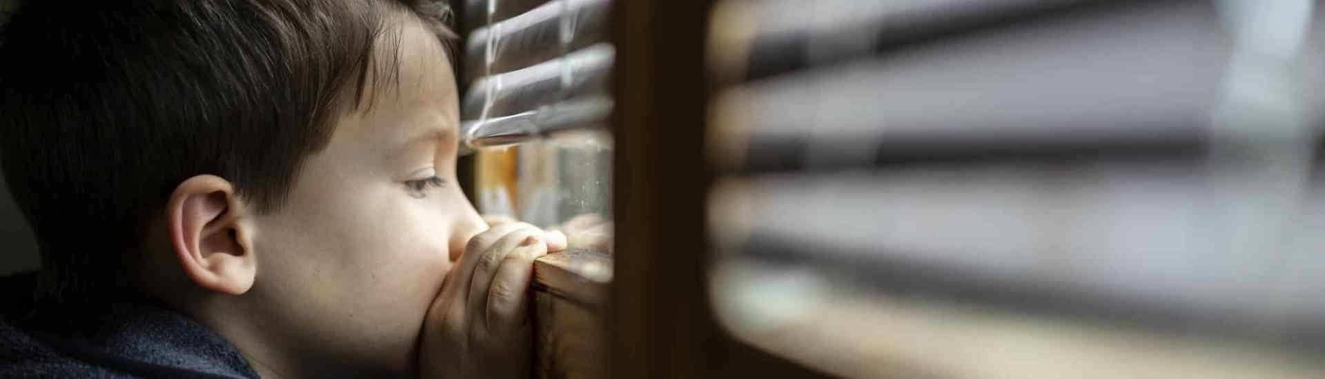 Rouwend kind kijkt door de kieren van een rolluik: zo help je kinderen bij verlies