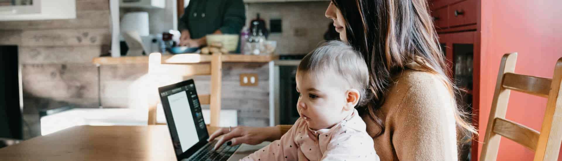 Mama met laptop en baby op schoot Thuiswerken met baby, peuter of kleuter